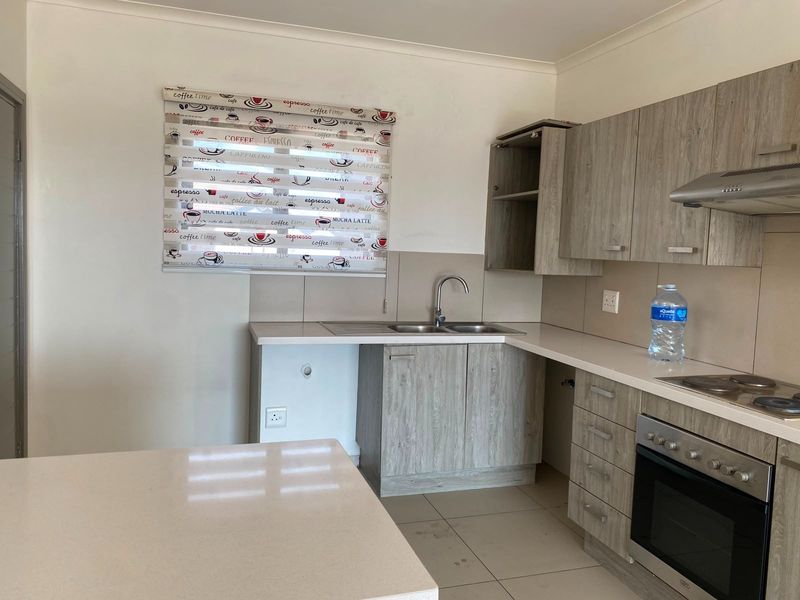 A functional kitchen featuring light wood-grain cabinetry, built-in oven with hob, and tiled splashbacks. The space is clean and ready for personalization.