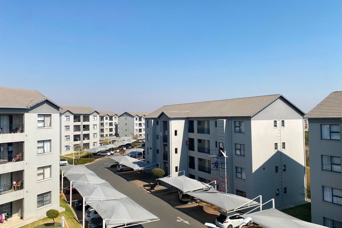 An elevated view of a modern apartment complex featuring multiple residential blocks, paved driveways, and covered parking structures under a clear blue sky.