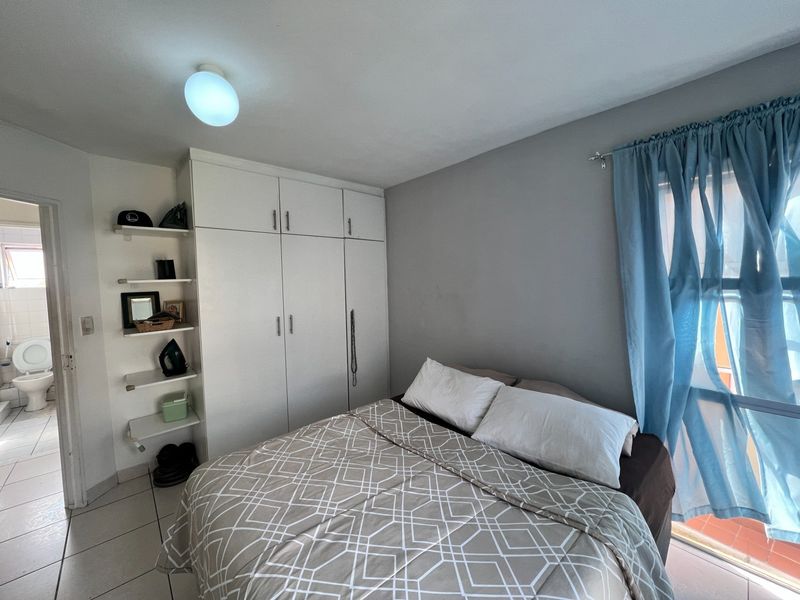A bedroom featuring built-in wardrobes, integrated shelving, and tiled flooring, with direct access to an adjacent bathroom.