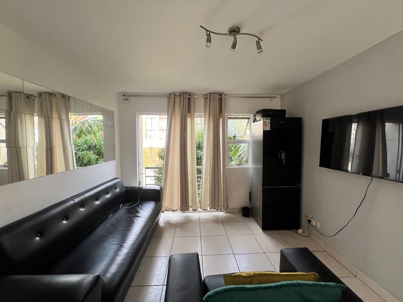 A living room featuring tiled flooring, a wall-mounted mirror, and a sliding glass door providing access to the exterior.