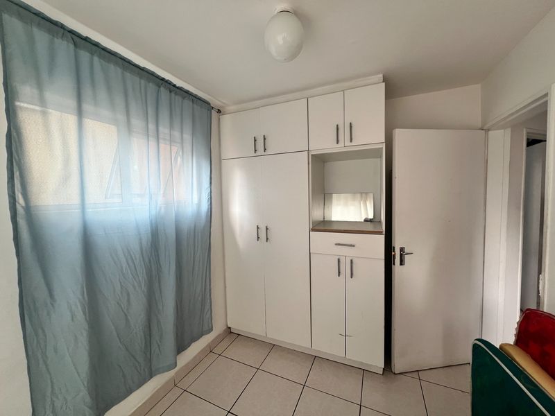 A functional bedroom featuring built-in white cupboards with integrated shelving and tiled flooring, offering a clean and neutral space ready for personalization.