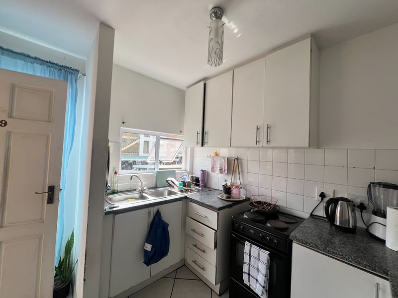 Compact kitchen featuring white cabinetry, laminate countertops, a double bowl sink, and a tiled splashback, providing a functional workspace.