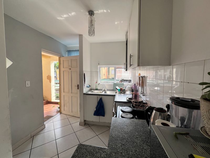 Compact kitchen featuring stone countertops, double bowl sink, tiled backsplash, and built-in cabinetry, with direct access to an exterior entrance area.