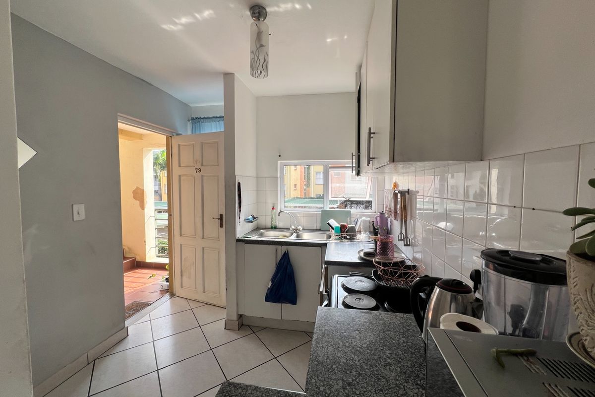 Compact kitchen featuring stone countertops, double bowl sink, tiled backsplash, and built-in cabinetry, with direct access to an exterior entrance area.