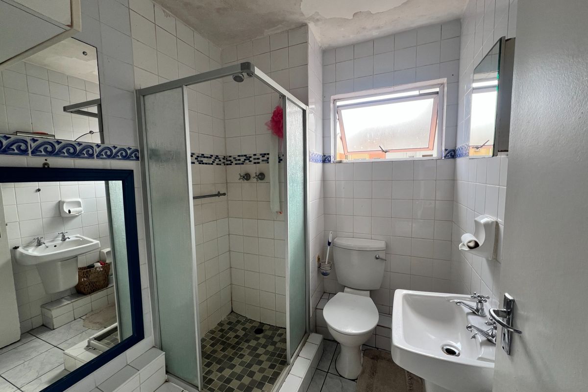 A functional bathroom featuring a shower enclosure, pedestal basin, and toilet, with tiled finishes and a window for ventilation.