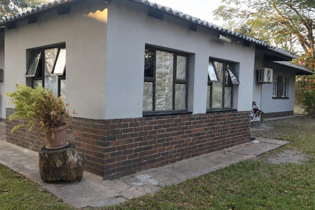 Rear exterior view of the house featuring a brick and plastered facade, aluminium window frames, and an installed air conditioning unit.
