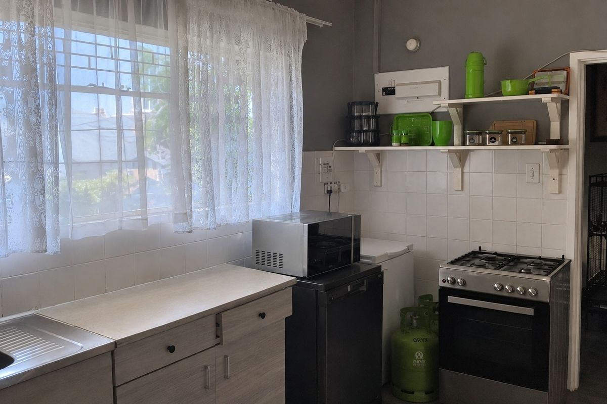 A functional kitchen featuring a gas stove, tiled splashback, stainless steel sink, and open wall shelving, providing a practical workspace with a neutral aesthetic.