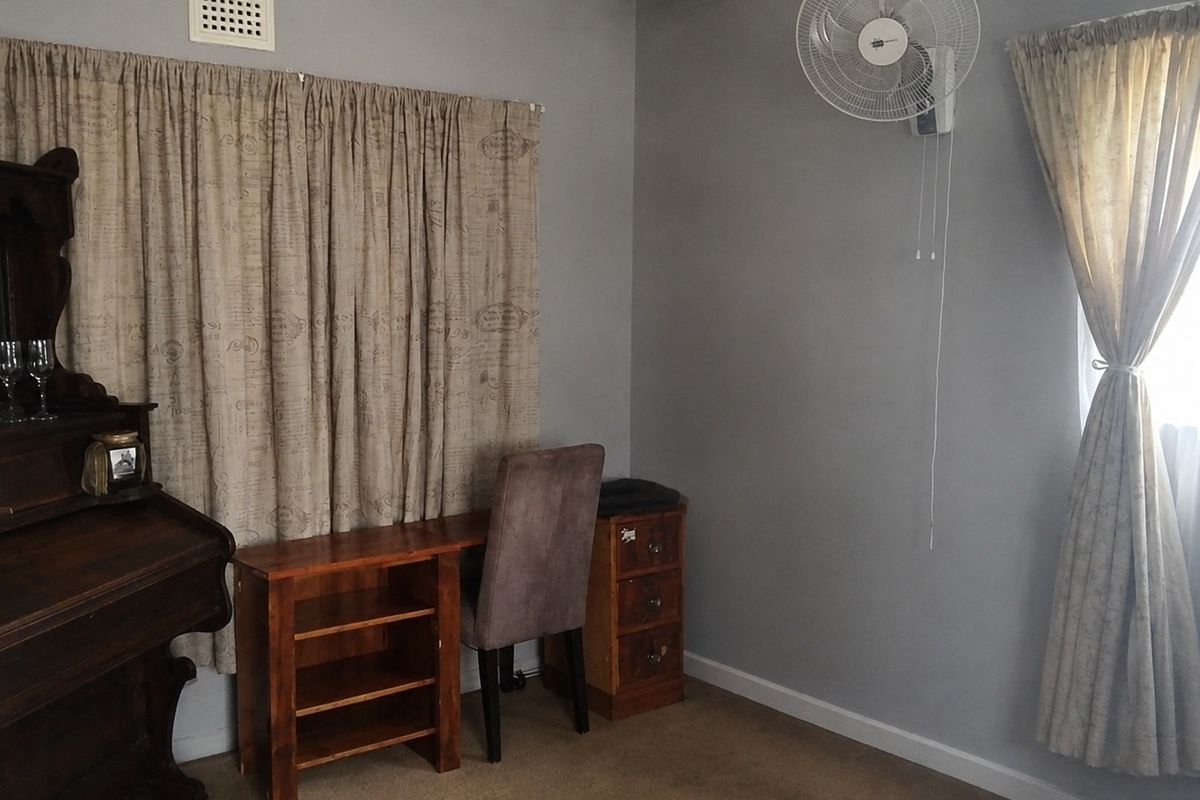 A bedroom featuring grey walls, carpet flooring, and a wall-mounted fan, providing a functional space with neutral finishes.