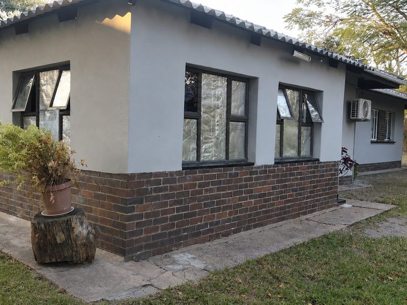 Rear exterior view of the house featuring a brick and plastered facade, aluminium window frames, and an installed air conditioning unit.