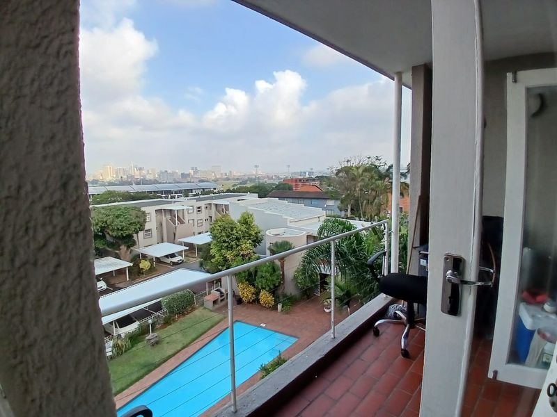 A balcony featuring tiled flooring and a metal railing, offering an elevated view of the complex pool area and surrounding cityscape.