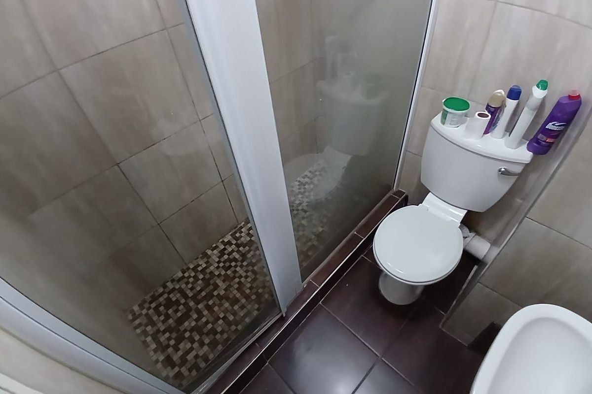 A functional bathroom featuring a shower enclosure with mosaic tiling, a standard toilet, and a bidet with dark ceramic floor tiles.