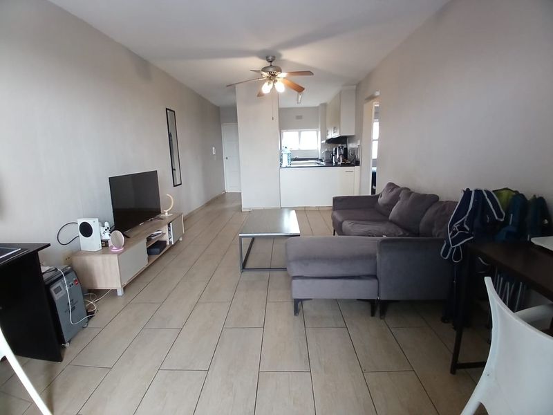 Open-plan living area featuring tiled flooring, a ceiling fan, and an adjoining kitchen space with built-in cabinetry.