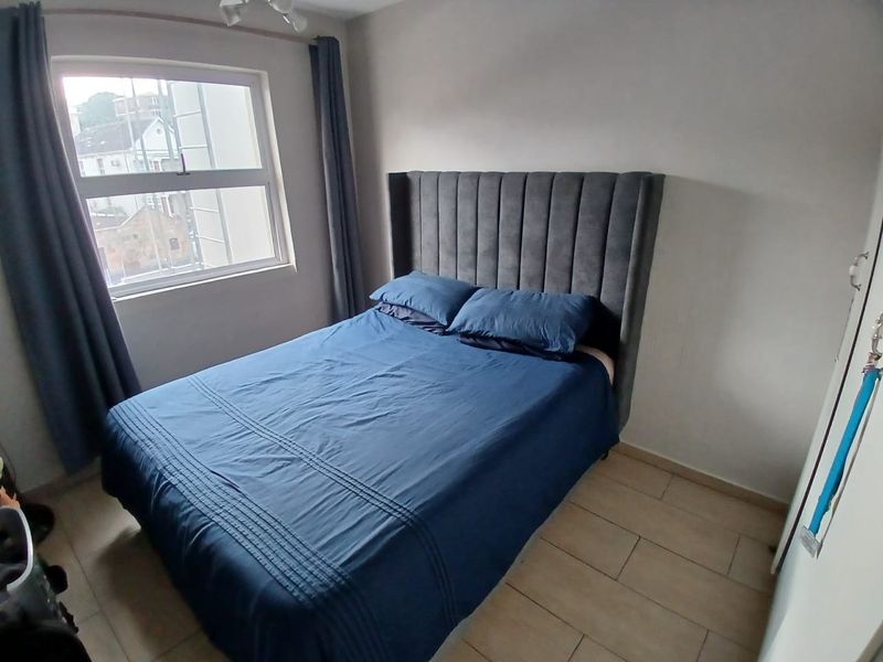 A well-lit bedroom featuring neutral tiled flooring and a large window, providing a clean and functional living space.