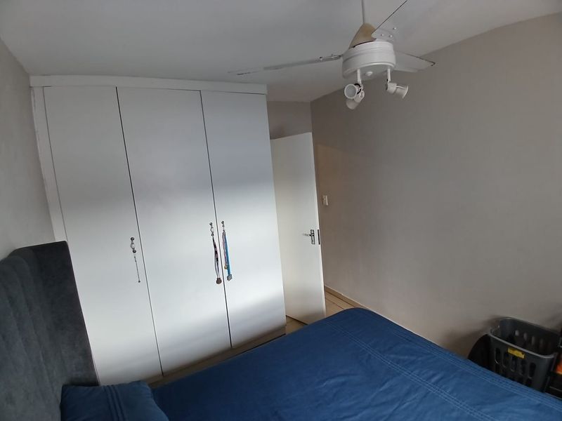 A bedroom featuring white built-in cupboards and a ceiling fan, providing functional storage and climate control.
