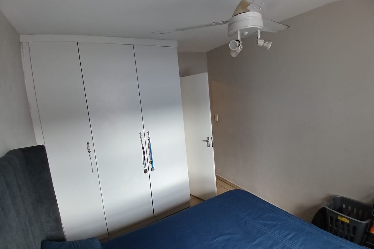 A bedroom featuring white built-in cupboards and a ceiling fan, providing functional storage and climate control.