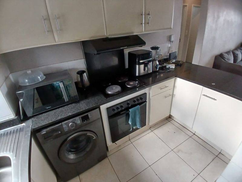 Compact kitchen featuring built-in cabinetry, electric hob, oven, extractor fan, and tiled flooring, offering a functional layout for daily meal preparation.