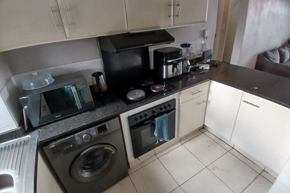 Compact kitchen featuring built-in cabinetry, electric hob, oven, extractor fan, and tiled flooring, offering a functional layout for daily meal preparation.