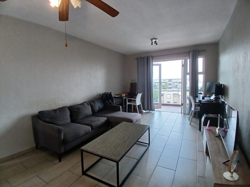 A living room featuring tiled flooring, a ceiling fan, and direct access to a balcony with a glass railing.