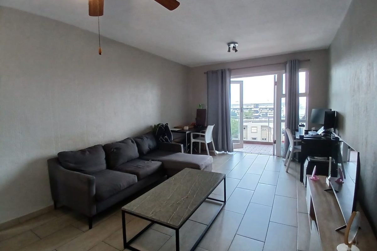 A living room featuring tiled flooring, a ceiling fan, and direct access to a balcony with a glass railing.