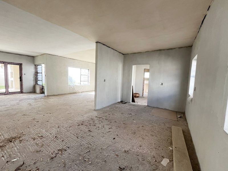An open-plan living area currently under construction, featuring plastered walls, aluminium window frames, and an unfinished floor surface ready for final finishes.