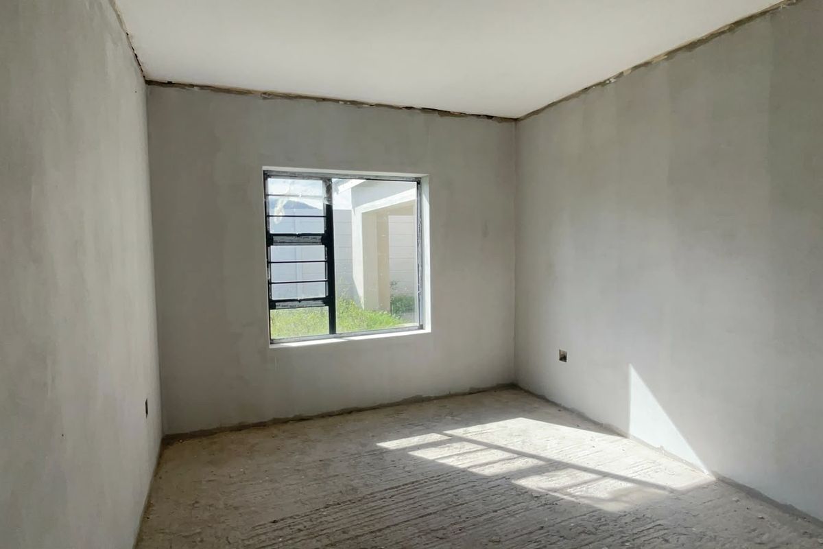 An unfinished bedroom space featuring plastered walls, a concrete floor, and an aluminium window frame, ready for final finishes and flooring installation.