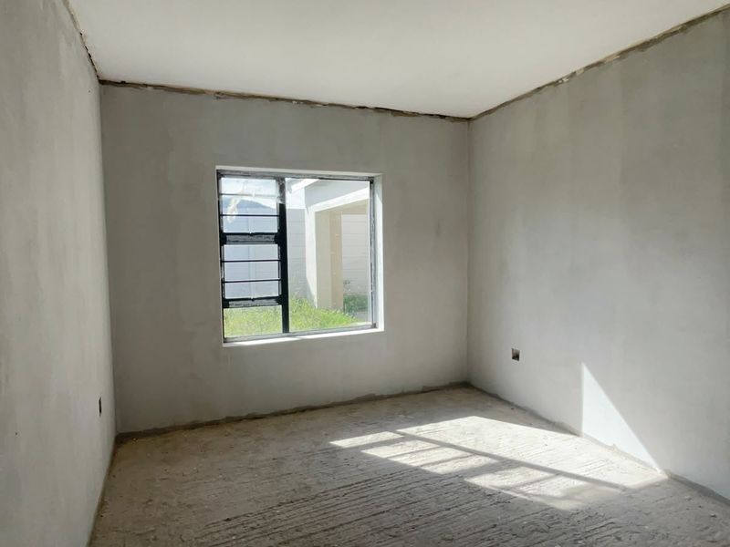 An unfinished bedroom space featuring plastered walls, a concrete floor, and an aluminium window frame, ready for final finishes and flooring installation.