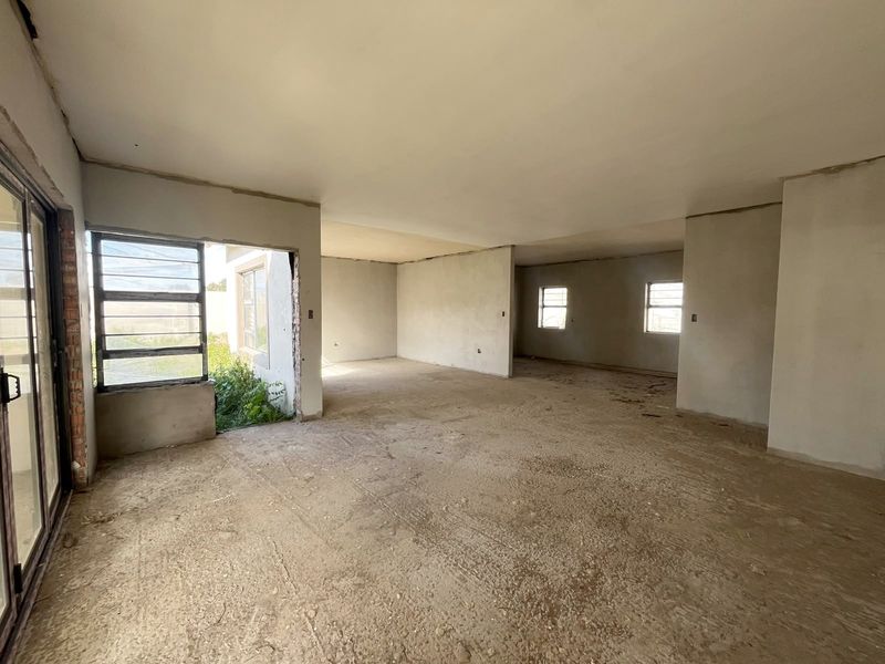 An expansive, open-plan living area in a shell state, featuring plastered walls, aluminium sliding doors, and large windows, ready for final flooring and finishes.
