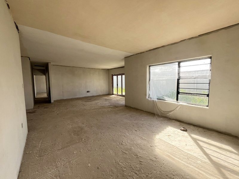 Spacious open-plan living area currently in a shell construction state, featuring plastered walls, large windows, and sliding doors awaiting final flooring and finishes.