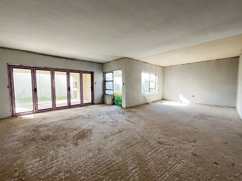 Spacious open-plan living area in a shell state, featuring large aluminium folding doors, multiple windows, and unfinished cement flooring ready for final finishes.
