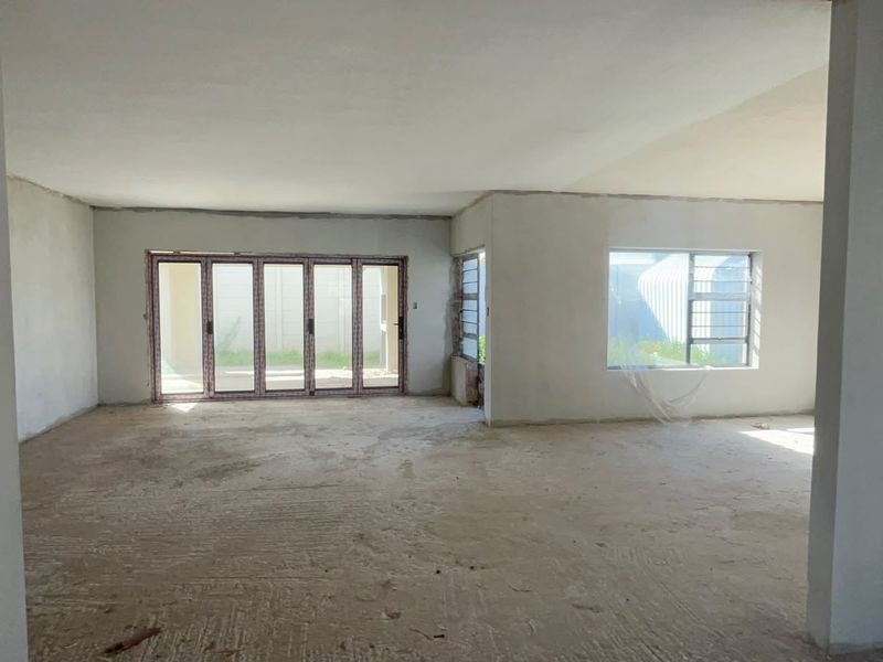 Spacious open-plan living area in a shell state, featuring large aluminium stacker doors and windows, ready for final flooring and interior finishes.