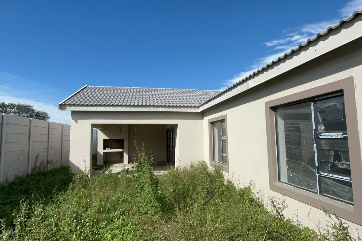 Rear view of the property featuring a covered patio with a built-in braai, concrete boundary wall, and overgrown garden area.