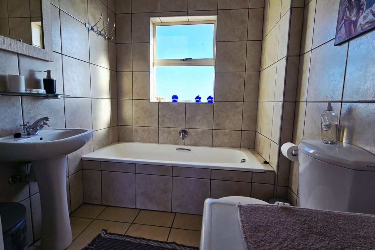 A functional bathroom featuring a pedestal basin, built-in bathtub, and neutral ceramic tiling throughout, offering a clean and practical layout.