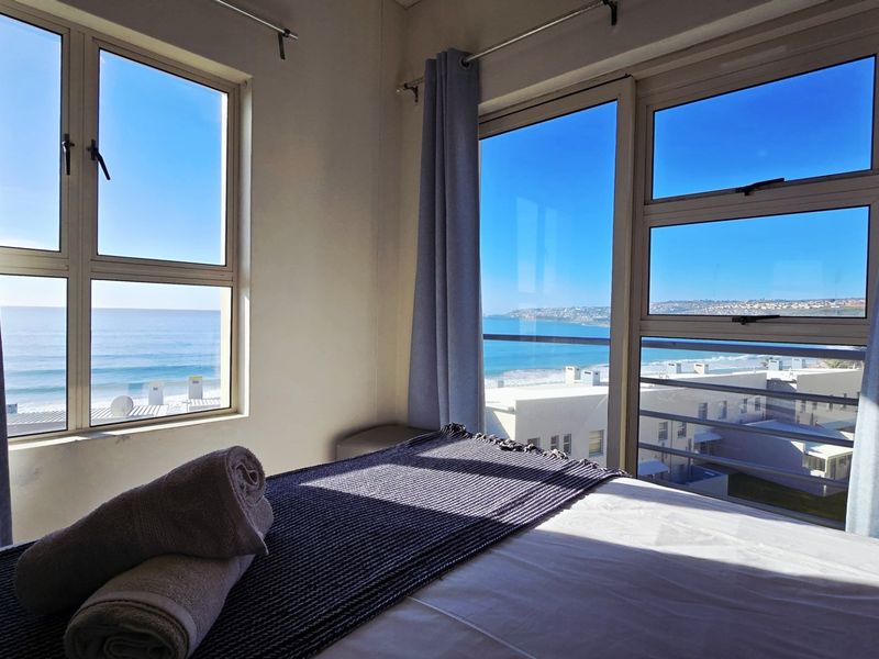 A bright bedroom featuring large windows and a sliding glass door that offers expansive ocean and coastal views.