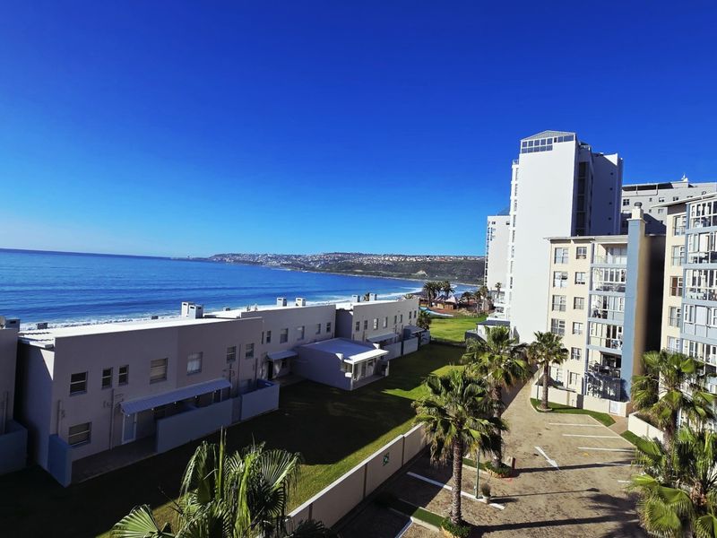 Elevated coastal view overlooking the apartment complex grounds, parking area, and the ocean coastline.