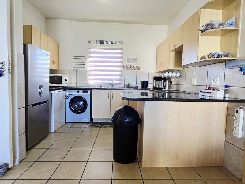 Functional kitchen featuring laminate cabinetry, granite countertops, tiled backsplash, and a breakfast bar, with integrated space for laundry appliances.
