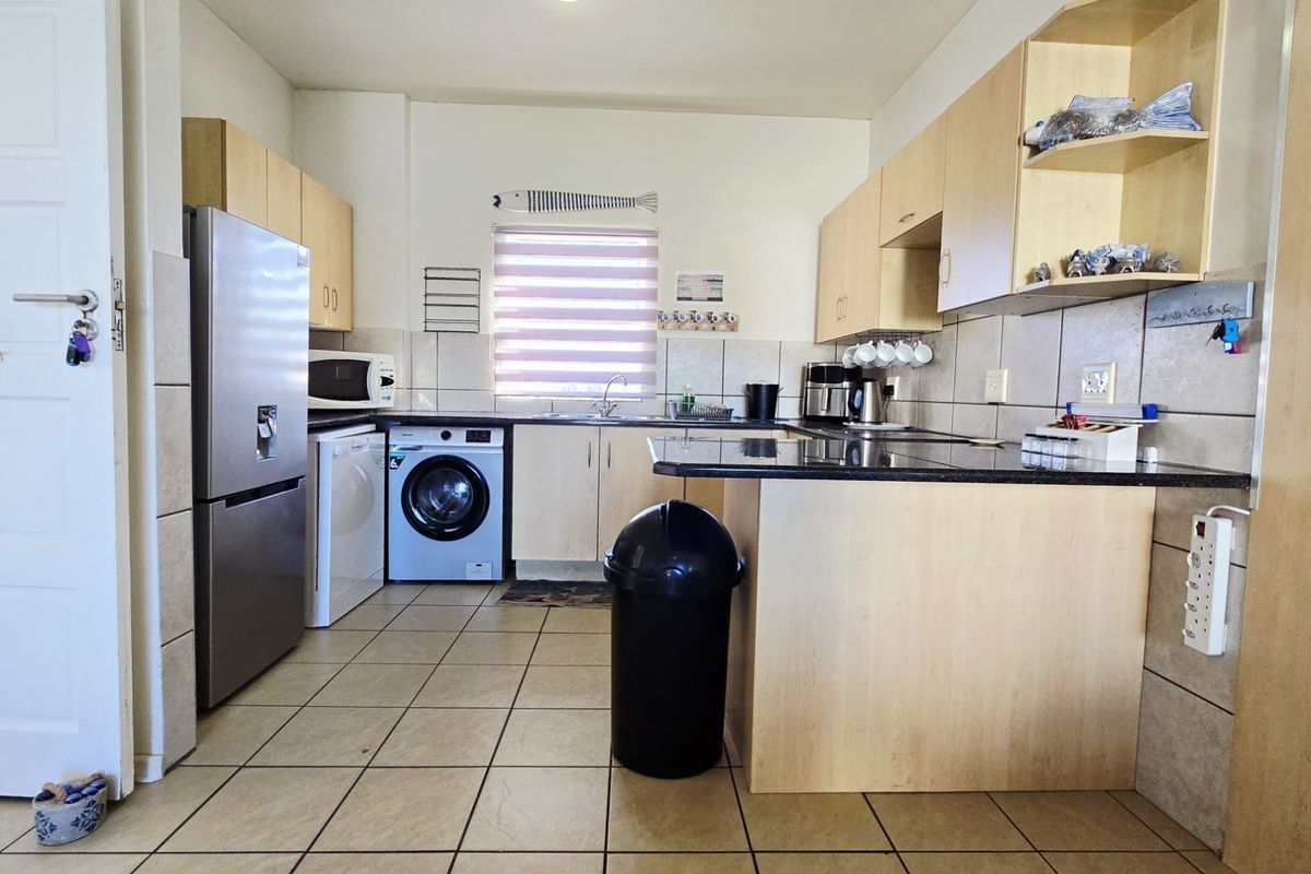 Functional kitchen featuring laminate cabinetry, granite countertops, tiled backsplash, and a breakfast bar, with integrated space for laundry appliances.