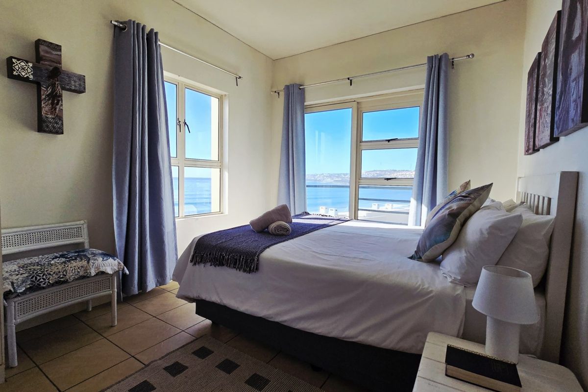 A bedroom featuring tiled flooring and large windows with ocean views, providing natural light and a coastal atmosphere.
