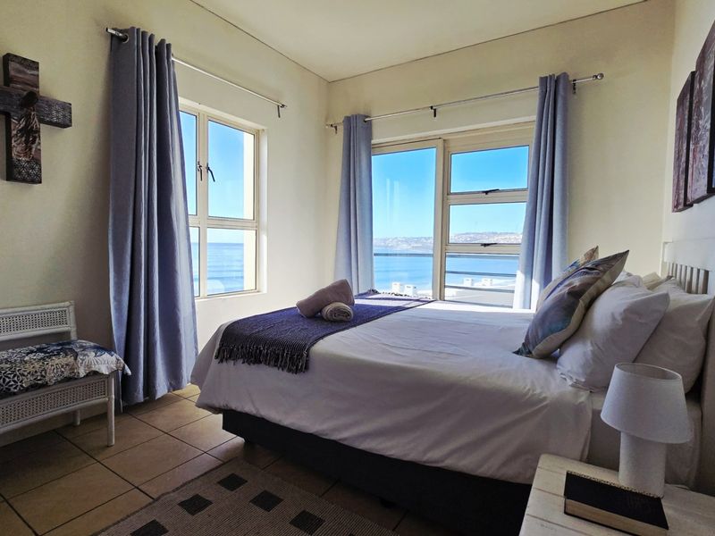 A bedroom featuring tiled flooring and large windows with ocean views, providing natural light and a coastal atmosphere.
