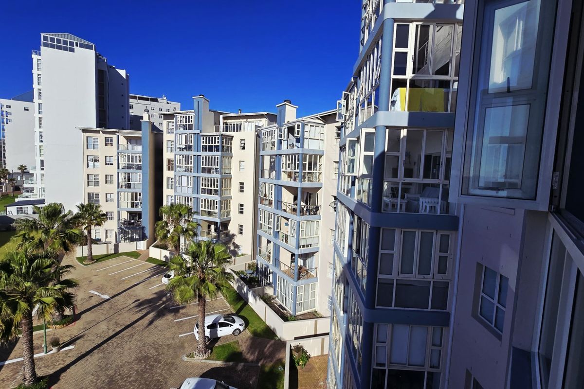 An elevated view of the apartment complex exterior, featuring paved parking, landscaped palm trees, and multiple residential balconies.