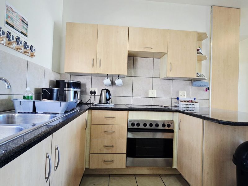 A functional kitchen featuring light wood laminate cabinetry, granite countertops, a built-in oven with electric hob, and a double bowl sink.