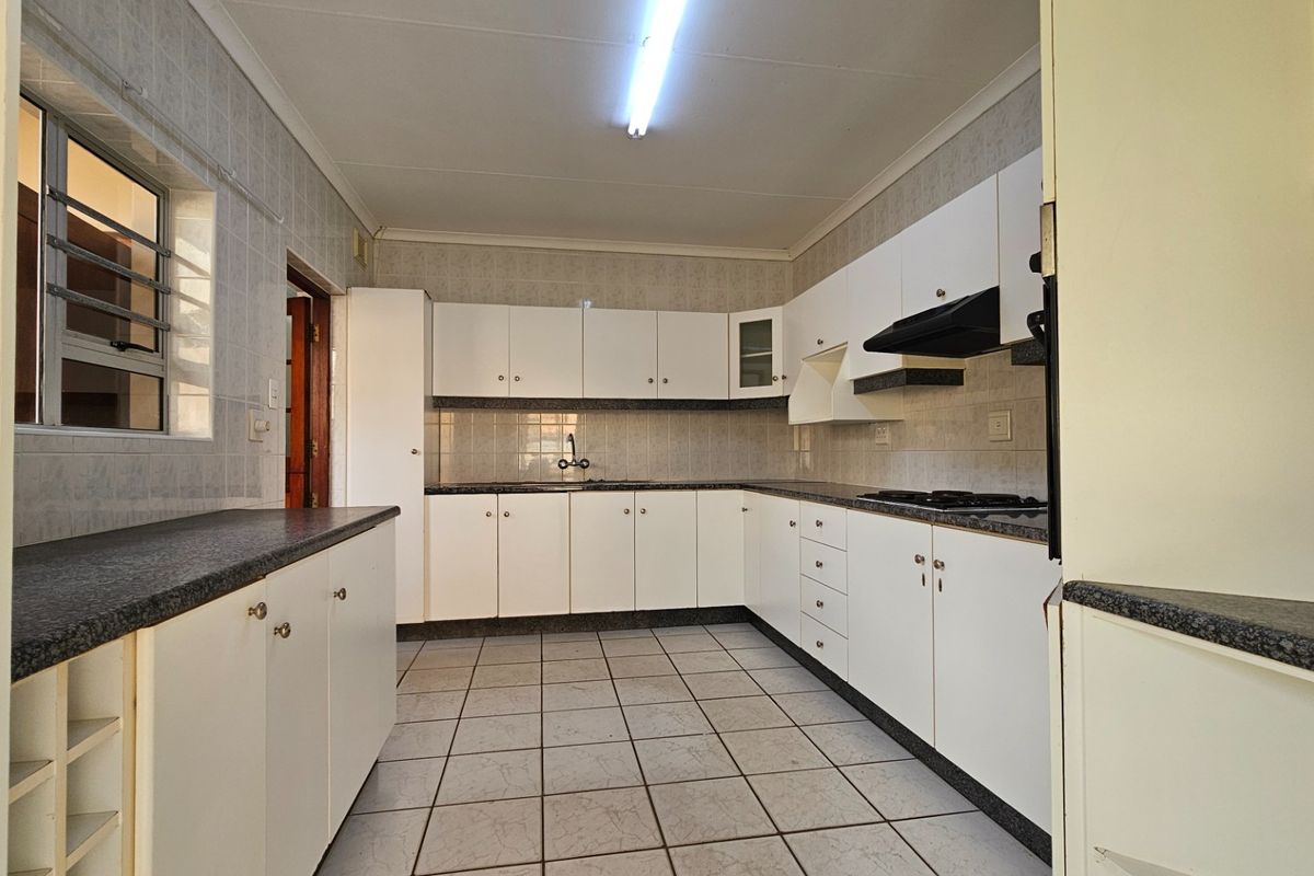 A functional, empty kitchen featuring white built-in cabinetry, dark laminate countertops, ceramic tile flooring, and a built-in hob with an extractor fan.