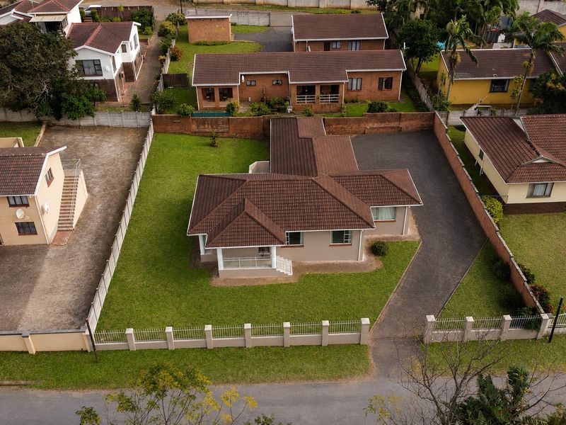 Aerial view of a residential property featuring a tiled roof, paved driveway, and surrounding lawn area within a fenced plot.