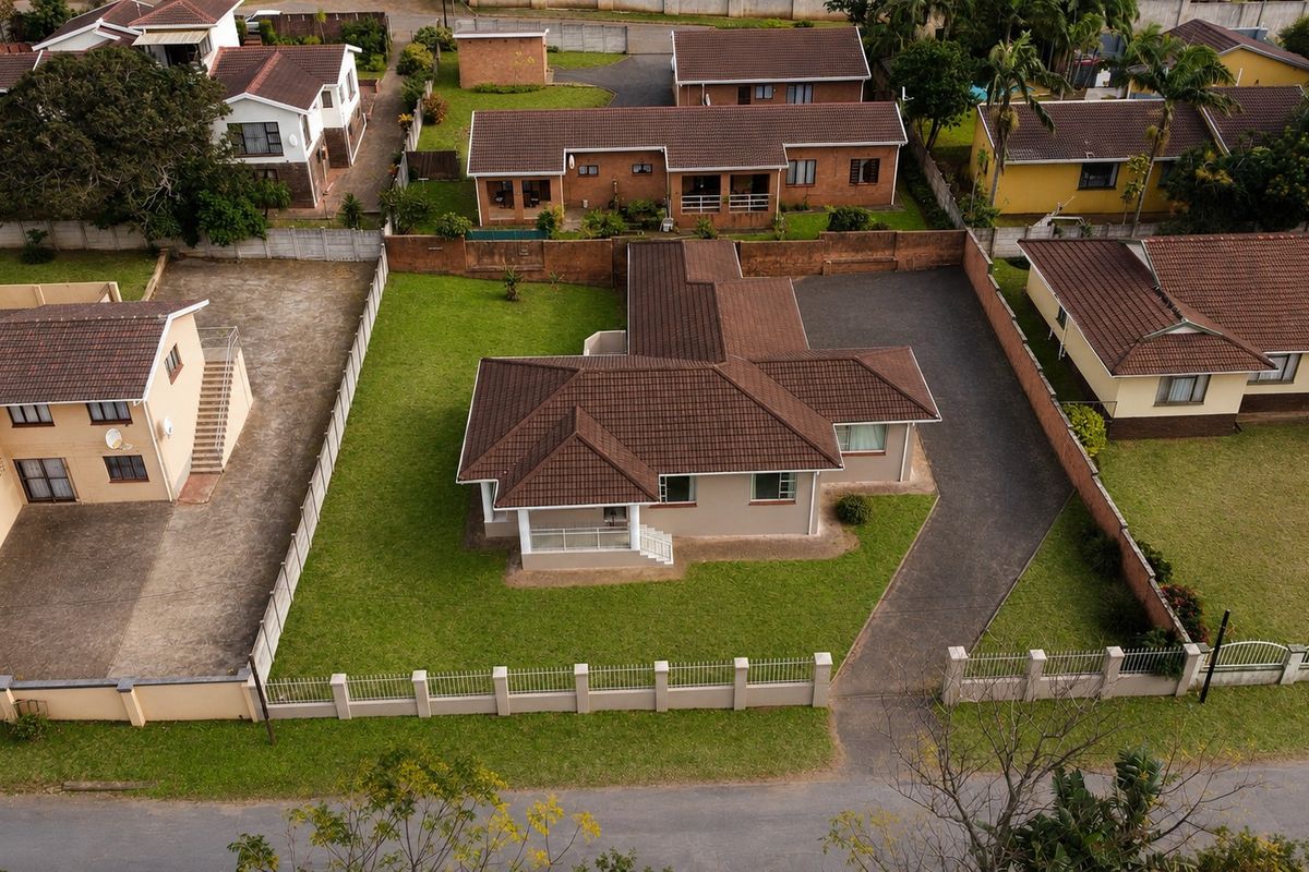 Aerial view of a residential property featuring a tiled roof, paved driveway, and surrounding lawn area within a fenced plot.