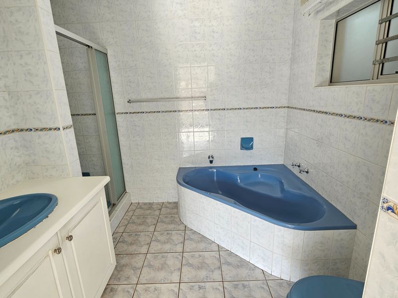A functional bathroom featuring a corner bathtub, vanity with integrated basin, and a separate shower enclosure with tiled finishes throughout.