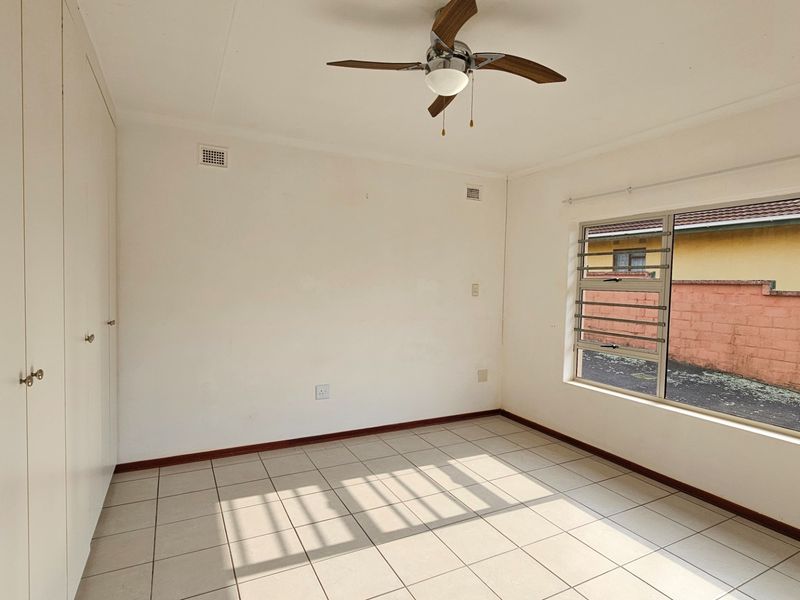 A bright, empty bedroom featuring tiled flooring, built-in cupboards, and a ceiling fan, offering a clean canvas for personalization.