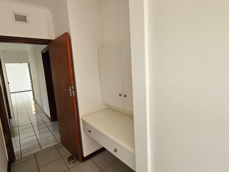 A bright hallway featuring tiled flooring and a built-in vanity unit with storage cabinetry.
