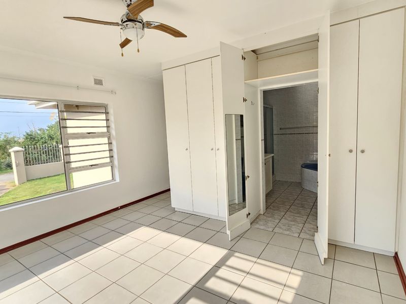 A bright, empty bedroom featuring built-in cupboards, tiled flooring, a ceiling fan, and direct access to an en-suite bathroom.
