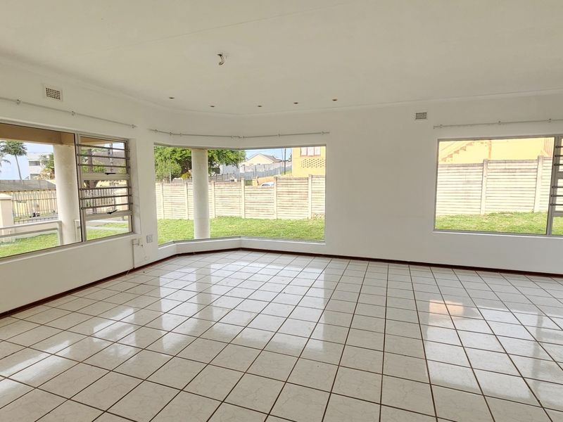 Spacious, light-filled living area featuring large windows, neutral tiled flooring, and recessed lighting, offering a blank canvas for interior design.