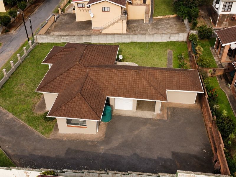 Aerial view of a residential property featuring a tiled roof, asphalt driveway, garage, and surrounding garden space within a fenced perimeter.