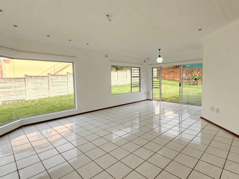 Spacious, light-filled living area featuring large windows, tiled flooring, and direct access to the rear garden through sliding glass doors.